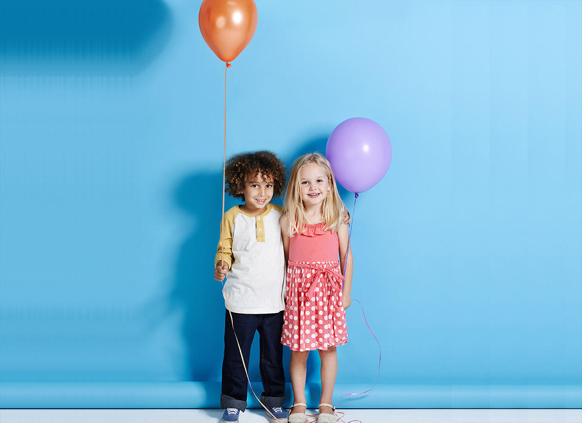 Deux enfants souriants tenant des ballons, un garçon avec un ballon orange et une fille avec un ballon violet, sur fond bleu pour l'offre We Love Family d'Appart'City.